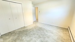 Interior room featuring neutral wall paint, light-toned carpet, white bi-fold closet doors, and baseboard heating - 