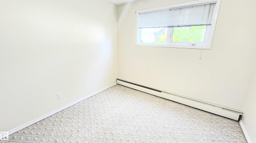 Bright room featuring a window with horizontal blinds, light-toned patterned carpeting, and white baseboard trim - 8824 90 Street, Edmonton, AB 