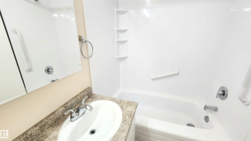 Bathroom featuring a white bathtub with integrated shelving, chrome fixtures, and grab bars - 8824 90 Street, Edmonton, AB 