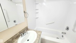 Bathroom featuring a white bathtub with integrated shelving, chrome fixtures, and grab bars - 
