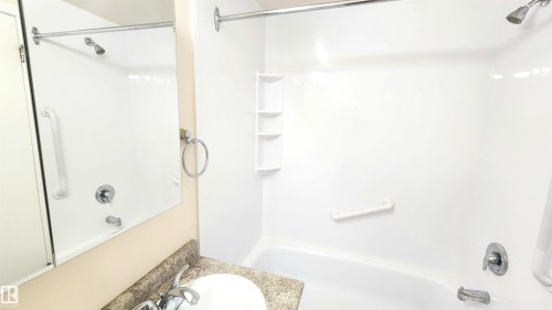 Bathroom featuring a combination shower and tub with a white surround, integrated shelving, and polished chrome fixtures - 8824 90 Street, Edmonton, AB 