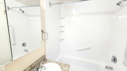 Bathroom featuring a combination shower and tub with a white surround, integrated shelving, and polished chrome fixtures - 