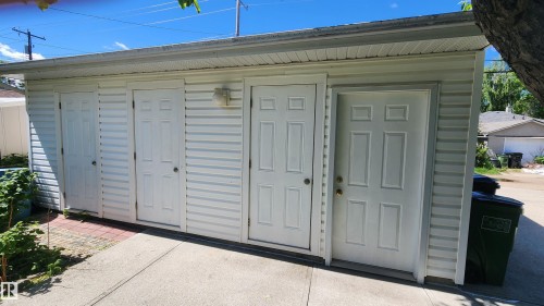 White vinyl-sided exterior structure featuring multiple entry doors, an attached overhead soffit, and a concrete pathway - 8824 90 Street, Edmonton, AB 