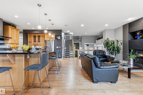 Open-concept living area featuring wood-finish flooring, a kitchen island with pendant lighting, stainless steel appliances, a modern fireplace, and an open staircase - 5709 Mcluhan Bay, Edmonton, AB 