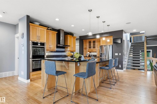 Kitchen featuring a large island with a dark countertop, light wood cabinetry, stainless steel appliances, and wood-finish flooring - 5709 Mcluhan Bay, Edmonton, AB 