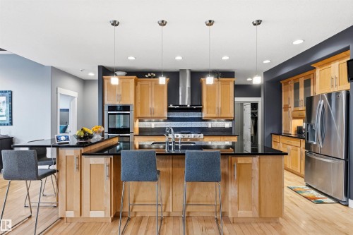 Open-concept kitchen featuring wood-finish flooring, light wood cabinetry, black countertops, and stainless steel appliances - 5709 Mcluhan Bay, Edmonton, AB 