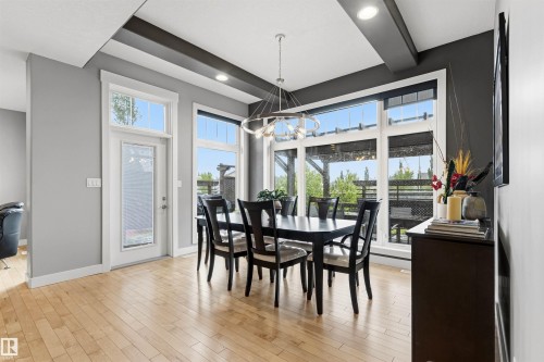 Bright dining area featuring hardwood flooring, extensive windows, a glass-panel exterior door, recessed lighting, and a contemporary chandelier - 5709 Mcluhan Bay, Edmonton, AB 