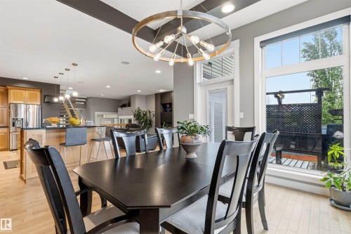 Dining area featuring a dark-toned table and chairs, light wood-finish flooring, and a contemporary circular chandelier - 5709 Mcluhan Bay, Edmonton, AB 