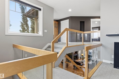 Multi-level interior featuring a contemporary glass and wood-finish railing system, a large window, a built-in recessed shelf, and recessed lighting - 5709 Mcluhan Bay, Edmonton, AB 