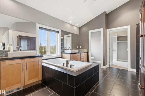 Spacious bathroom featuring an integrated soaking tub, dual vanity areas with vessel sinks, dark tile flooring, and a vaulted ceiling - 5709 Mcluhan Bay, Edmonton, AB 