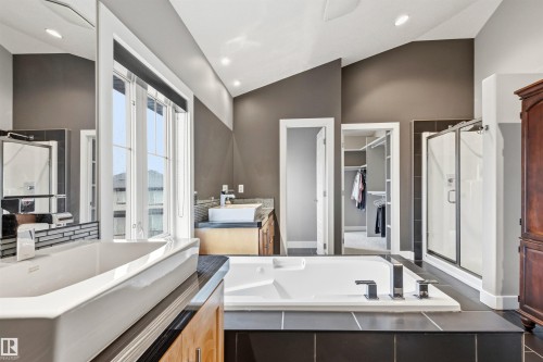 Bathroom featuring a built-in soaking tub, a glass-enclosed shower, dual vessel sinks with wall-mounted faucets, and a walk-in closet - 5709 Mcluhan Bay, Edmonton, AB 