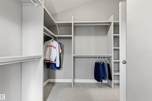 Walk-in closet featuring built-in shelving, multiple hanging rods, and light-toned carpeting - 5709 Mcluhan Bay, Edmonton, AB 