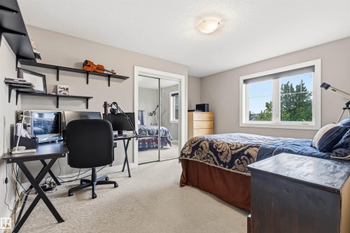 Carpeted room with a window providing natural light, featuring a modern ceiling light fixture, mirrored closet doors, and multiple wall-mounted shelves - 5709 Mcluhan Bay, Edmonton, AB 