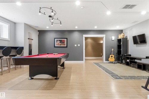 Spacious entertainment area featuring wood-finish flooring, recessed lighting, and a modern track light fixture - 5709 Mcluhan Bay, Edmonton, AB 