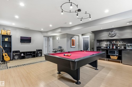 Spacious entertainment room featuring light wood-finish flooring, recessed lighting, and a built-in wet bar with stainless steel appliances - 5709 Mcluhan Bay, Edmonton, AB 