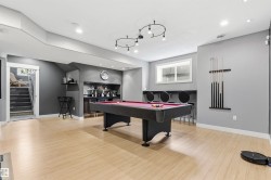 Open recreation space featuring light wood-finish flooring, recessed lighting, and a built-in wet bar with dark cabinetry - 
