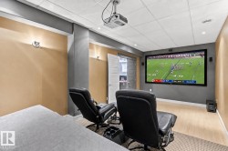 Dedicated media room featuring a large projection screen, ceiling-mounted projector, recessed lighting, and sconce lighting - 