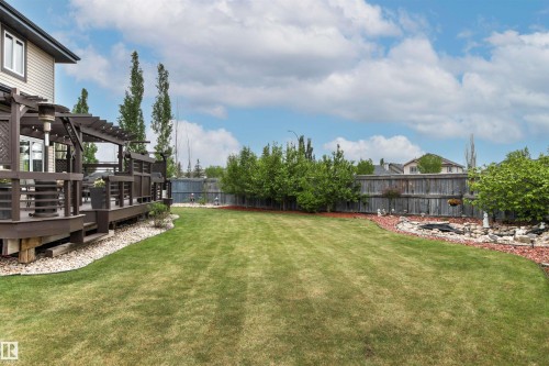 Expansive backyard featuring a large grassy lawn, a multi-level deck with a pergola, a rock garden with a pond, and mature landscaping - 5709 Mcluhan Bay, Edmonton, AB 