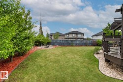 Expansive backyard featuring a lush lawn, a composite deck with pergola, and a decorative rock garden - 