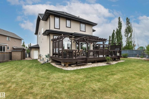 Rear exterior featuring a multi-level wood deck with pergola, expansive lawn, and gravel landscaping - 5709 Mcluhan Bay, Edmonton, AB 