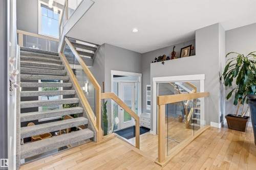 Grand entryway featuring a carpeted staircase with light wood and glass railings - 5709 Mcluhan Bay, Edmonton, AB 