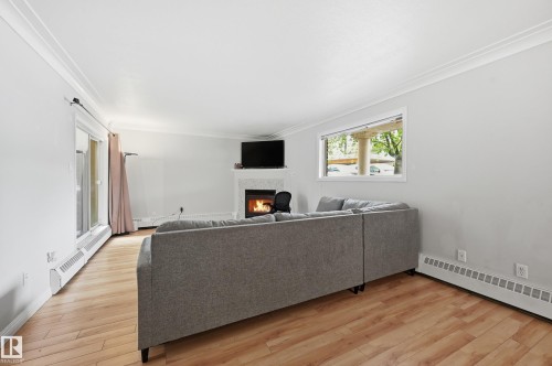 Living area featuring wood-finish flooring, a fireplace with a light-colored mantel, a large window, and crown molding - 33 9914 80 Avenue, Edmonton, AB - Indoor With Fireplace