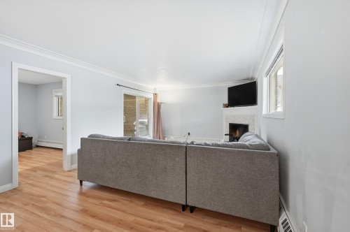 Living area featuring wood-finish flooring, a fireplace with a light-toned surround, a sliding glass door, and crown molding - 33 9914 80 Avenue, Edmonton, AB - Indoor Photo Showing Other Room With Fireplace