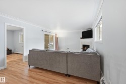 Living area featuring wood-finish flooring, a fireplace with a light-toned surround, a sliding glass door, and crown molding - 