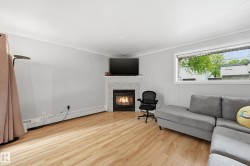 Living space featuring wood-finish flooring, a white trim fireplace with a tiled surround, a large window providing natural light, crown molding, and light gray wall paint - 