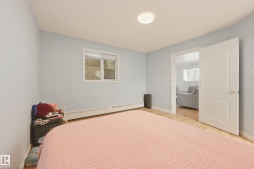 Bedroom featuring light blue walls, wood-finish flooring, a baseboard heating unit, and a window with blinds - 33 9914 80 Avenue, Edmonton, AB - Indoor