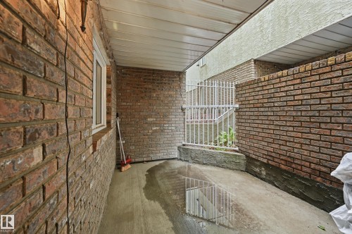 Brick exterior wall with a white-framed window, concrete flooring, and a white metal gate - 33 9914 80 Avenue, Edmonton, AB -  With Exterior
