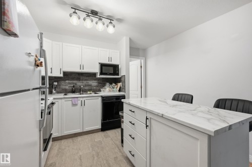 Kitchen featuring white cabinetry, a white marble-patterned countertop island with integrated storage, a dark tile backsplash, and light wood-finish flooring - 33 9914 80 Avenue, Edmonton, AB - Indoor Photo Showing Kitchen