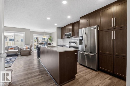 Modern kitchen featuring dark wood-finish cabinetry, stainless steel appliances, and a central island with a light-toned countertop - 223 40A Avenue, Edmonton, AB - Indoor Photo Showing Kitchen