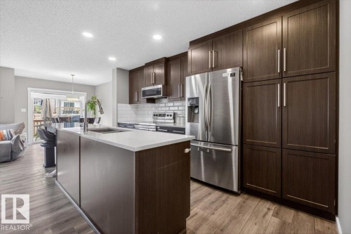 Contemporary kitchen featuring dark wood-finish cabinetry, stainless steel appliances, a white subway tile backsplash, and a large island with a surface-mounted sink and bar seating - 223 40A Avenue, Edmonton, AB - Indoor Photo Showing Kitchen With Upgraded Kitchen