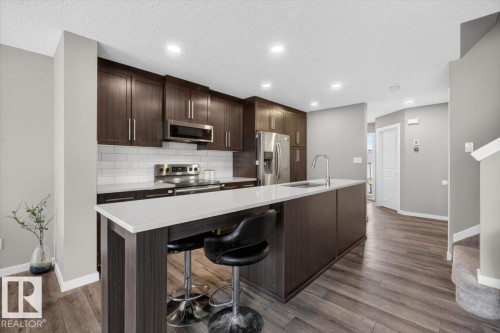 Modern kitchen featuring dark wood-finish cabinetry, white subway tile backsplash, stainless steel appliances, and an expansive island with a white countertop - 223 40A Avenue, Edmonton, AB - Indoor Photo Showing Kitchen With Upgraded Kitchen
