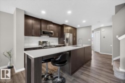 Modern kitchen featuring dark wood-finish cabinetry, white subway tile backsplash, stainless steel appliances, and an expansive island with a white countertop - 