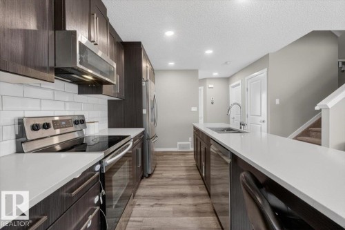 Contemporary kitchen with dark wood-finish cabinetry, stainless steel appliances, white subway tile backsplash, and light-toned countertops - 223 40A Avenue, Edmonton, AB - Indoor Photo Showing Kitchen With Double Sink With Upgraded Kitchen
