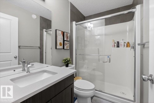 Bathroom featuring a dark wood-finish vanity with a light countertop, an integrated rectangular sink, a polished chrome faucet, a spacious mirror, and a glass-enclosed shower with a white surround - 223 40A Avenue, Edmonton, AB - Indoor Photo Showing Bathroom