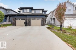 Contemporary exterior featuring dark siding, stone accents, and two light-colored garage doors - 
