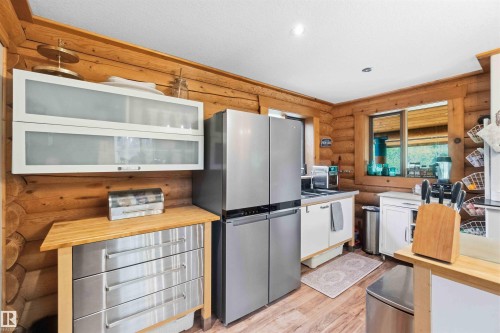 Kitchen featuring log wall construction, wood-finish flooring, a stainless steel refrigerator, white cabinetry, and a window with a wood frame - #17 A 15031 Twp Road 462, Rural Wetaskiwin County, AB - Indoor Photo Showing Kitchen