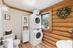 Laundry area featuring stacked appliances, log-style wall, wood-finish flooring, and a large window - 