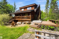Wood-sided dwelling with a dark metal roof, featuring a covered porch, an exterior staircase, a ground-level patio, and an adjacent wood deck with an integrated hot tub - 
