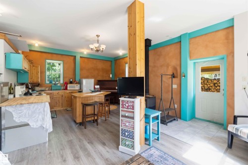 Open-concept living space featuring wood-finish flooring, a kitchen with natural wood cabinetry and a central island, and a wood-burning stove with a black stovepipe - #17 A 15031 Twp Road 462, Rural Wetaskiwin County, AB - Indoor
