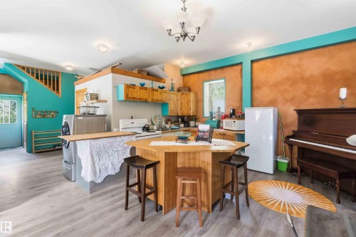 Open-concept living space featuring wood-finish flooring, a central kitchen island with seating, a built-in staircase, and light wood cabinetry - #17 A 15031 Twp Road 462, Rural Wetaskiwin County, AB - Indoor