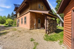 Two-story exterior with a stucco finish on the lower level and wood siding on the upper level, featuring solar panels, a covered patio area, and a gravel ground cover - 