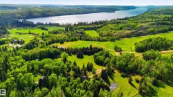 Expansive natural landscape featuring a large body of water, lush green trees, rolling hills, and open fields - 