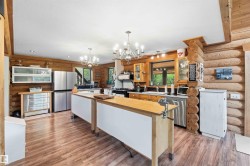Spacious kitchen featuring two island work surfaces with butcher block tops, stainless steel appliances, wood-finish flooring, exposed log walls, and two multi-arm chandeliers - 