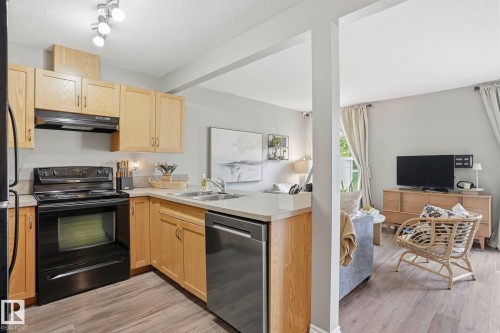 Kitchen featuring light wood cabinetry, black appliances, a stainless-steel dishwasher, and light-toned countertops - 164 150 Edwards Drive, Edmonton, AB - Indoor Photo Showing Kitchen With Double Sink