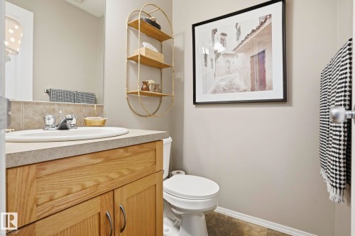 Bathroom featuring a wood-finish vanity with an integrated sink, a neutral countertop, and a tiled backsplash - 164 150 Edwards Drive, Edmonton, AB - Indoor Photo Showing Bathroom