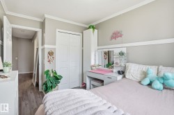 Bedroom featuring wood-finish flooring, neutral wall paint, white crown molding, and a paneled bifold closet door - 